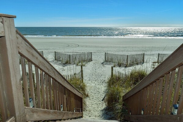 A wooden staircase leading to a sandy beach with a clear view of the ocean.
