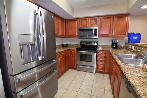 A modern kitchen with stainless steel appliances, wooden cabinets, granite countertops, and a built-in dishwasher.