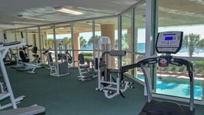 Un gimnasio con diferentes equipos de ejercicio, una cinta de correr y vistas a una piscina a través de amplias ventanas.