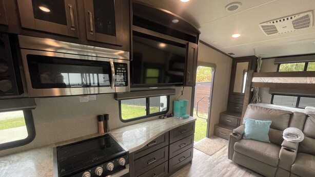 A compact RV kitchen with a stove, oven, microwave, and a small dining area.