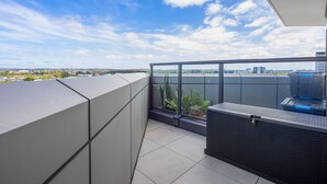 En balkon med udsigt over byens skyline, gelænder i glas og et lille siddeområde med bord og stole.