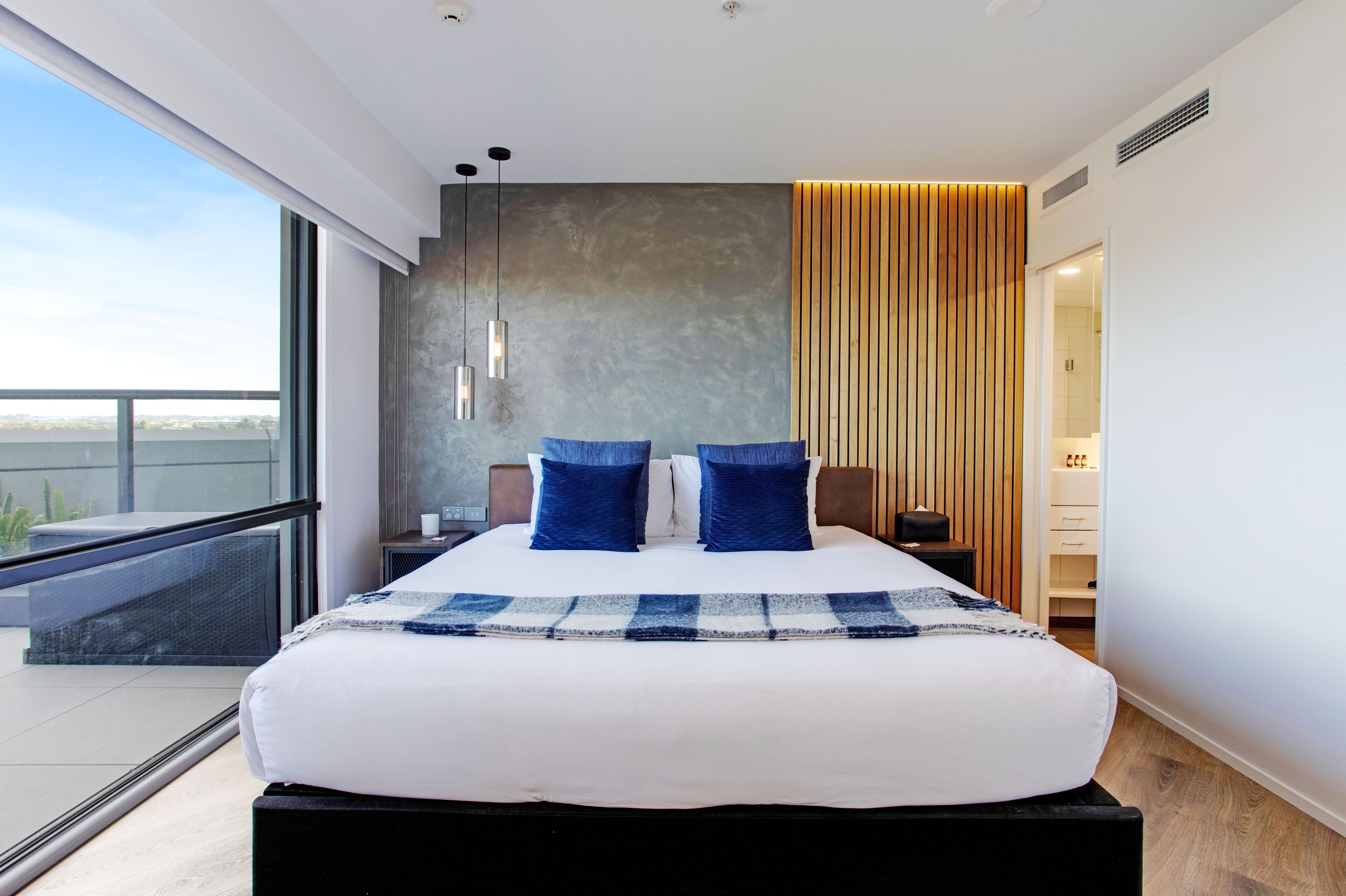A modern hotel room with a large bed, a balcony, and a view of the city.