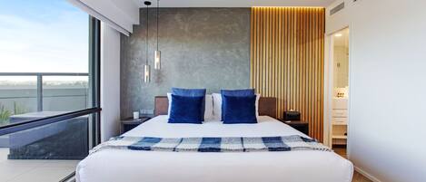 A modern hotel room with a large bed, a balcony, and a view of the city.