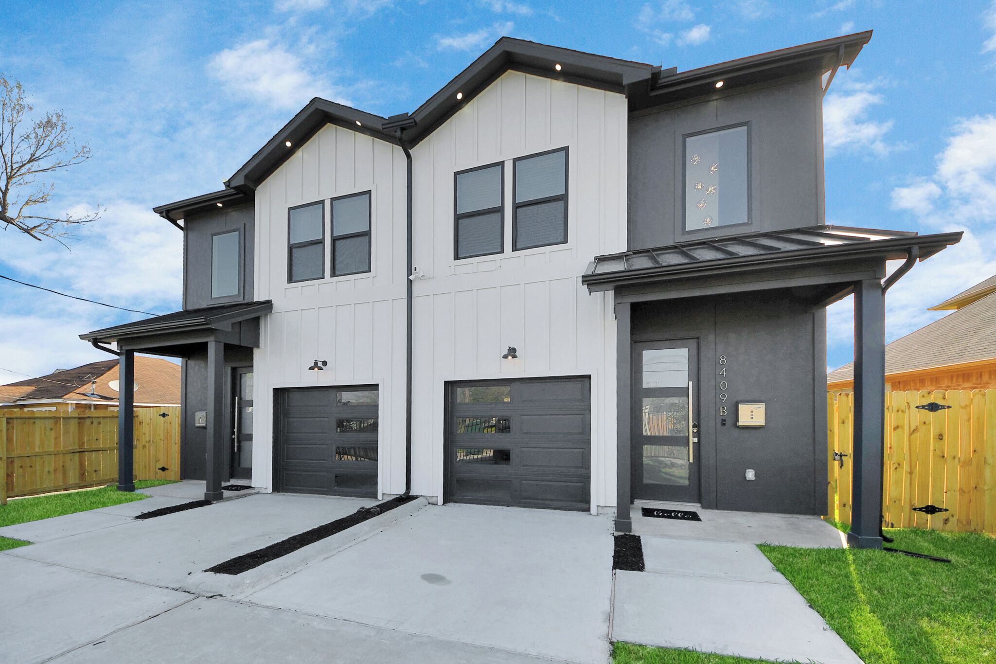 A two-story residential building with a garage, a covered porch, and a well-maintained lawn.