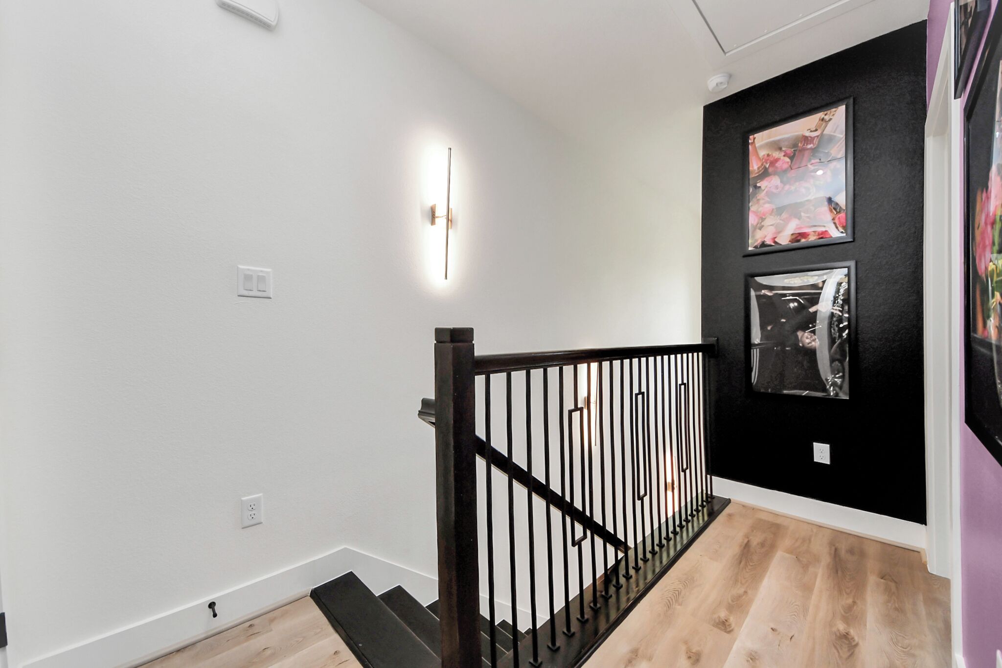 A staircase with a black railing leading to a room with white walls and a black accent wall with framed pictures.