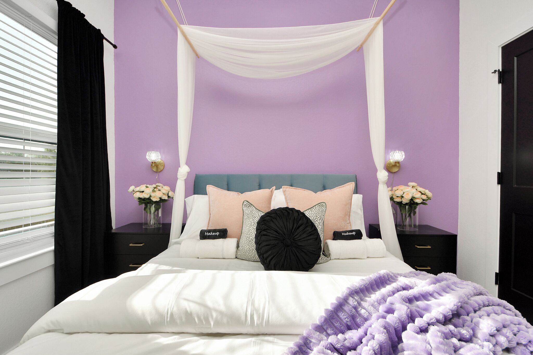 Ein Schlafzimmer mit Baldakinsbett, zwei Nachttischen mit Lampen und einer violetten Wand.