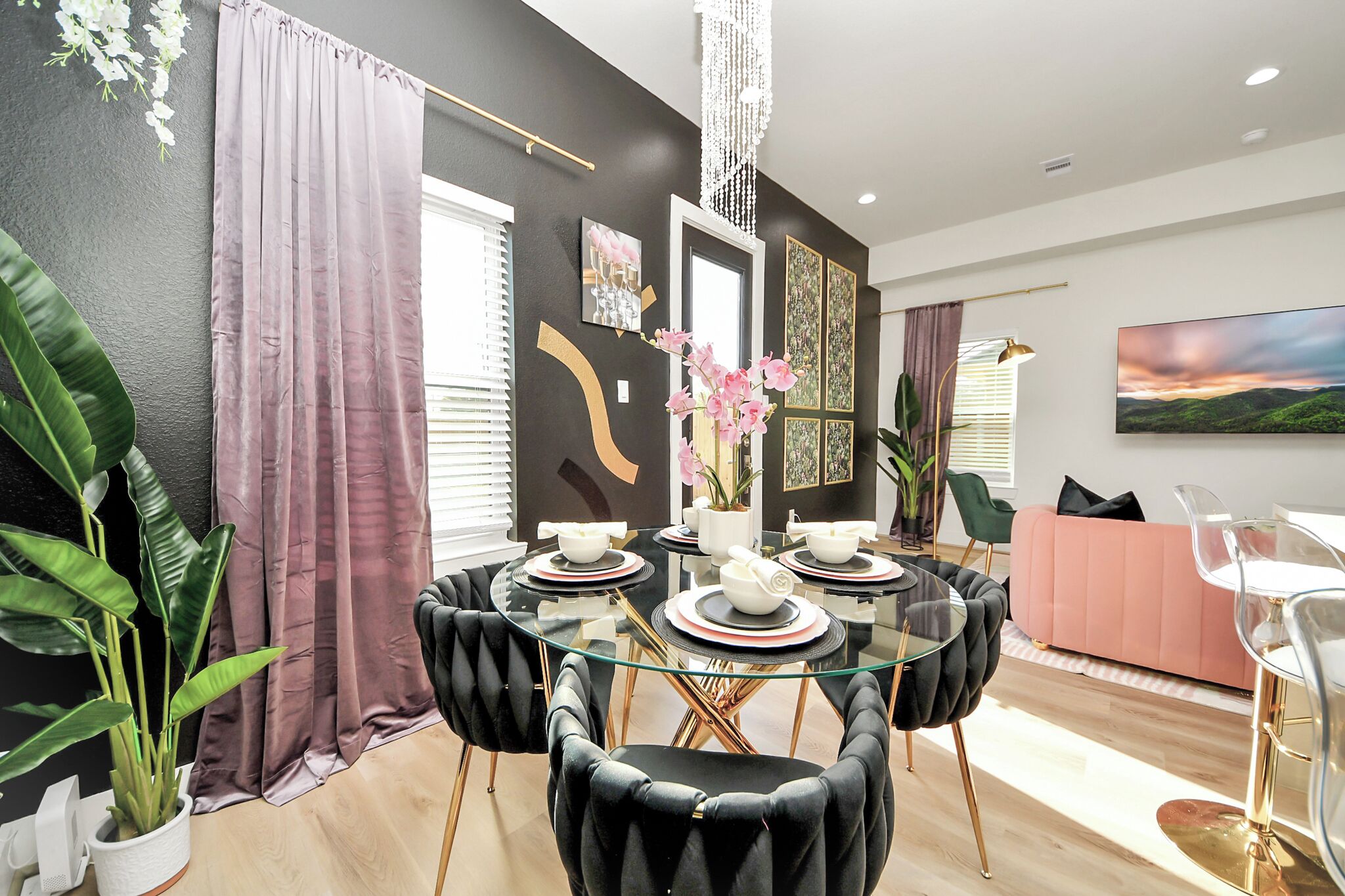 Un espace repas moderne avec une table en verre, des chaises à revêtement noir et un canapé rose.