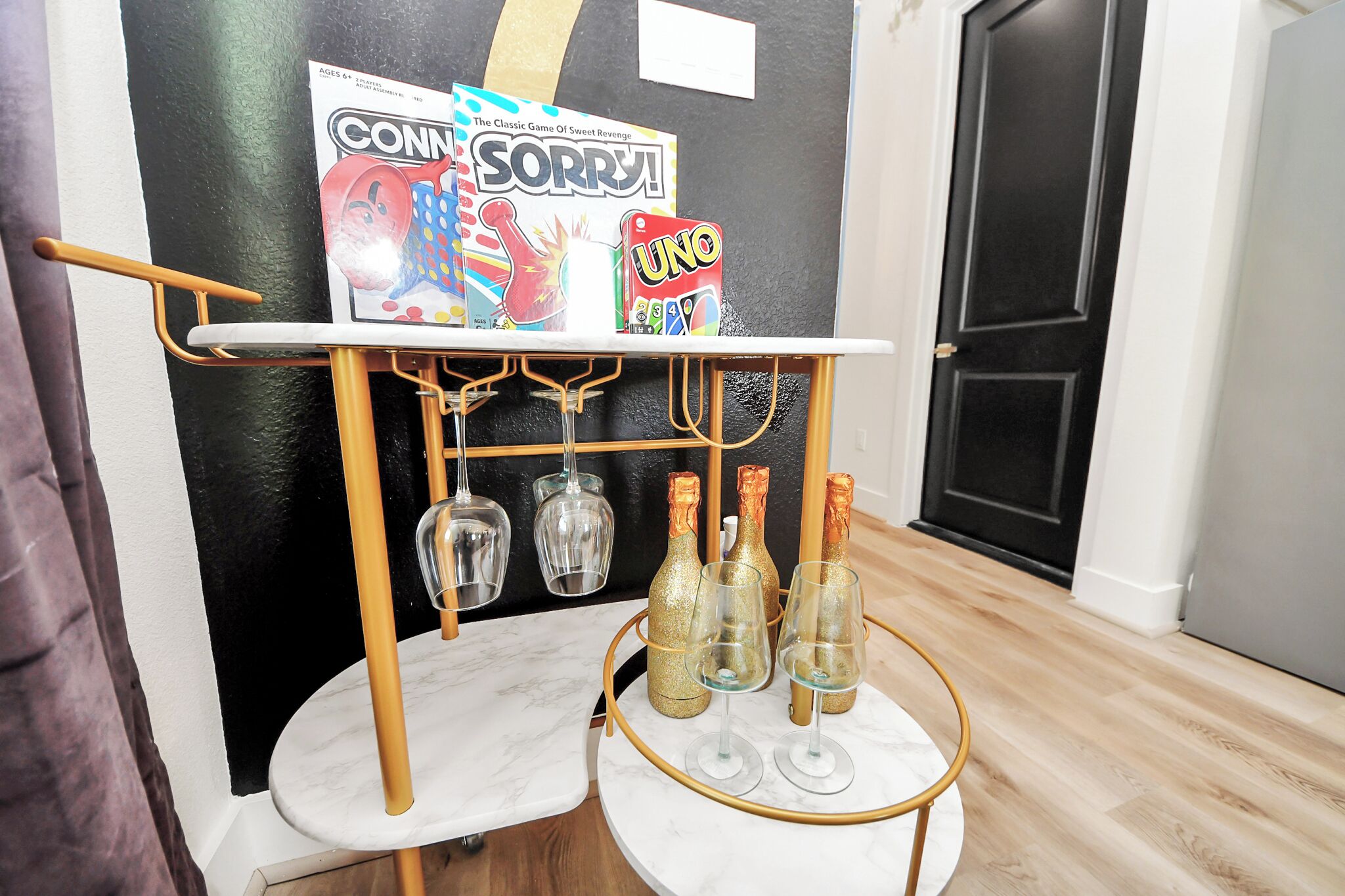 Un carrito bar con botellas y copas, un tablero de juego y una puerta al fondo.