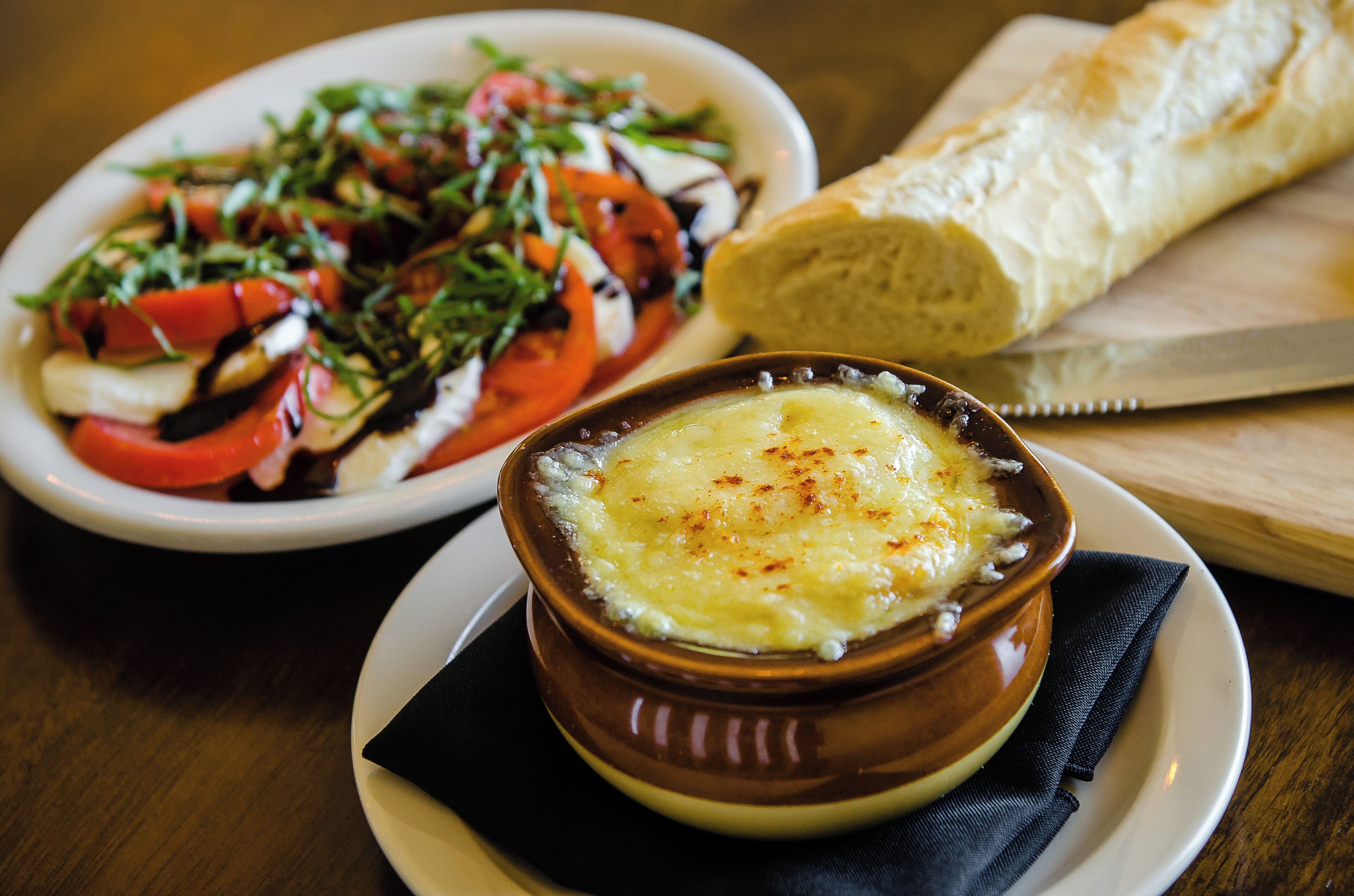 A bowl of French onion soup and a plate of salad with a baguette on a wooden table.