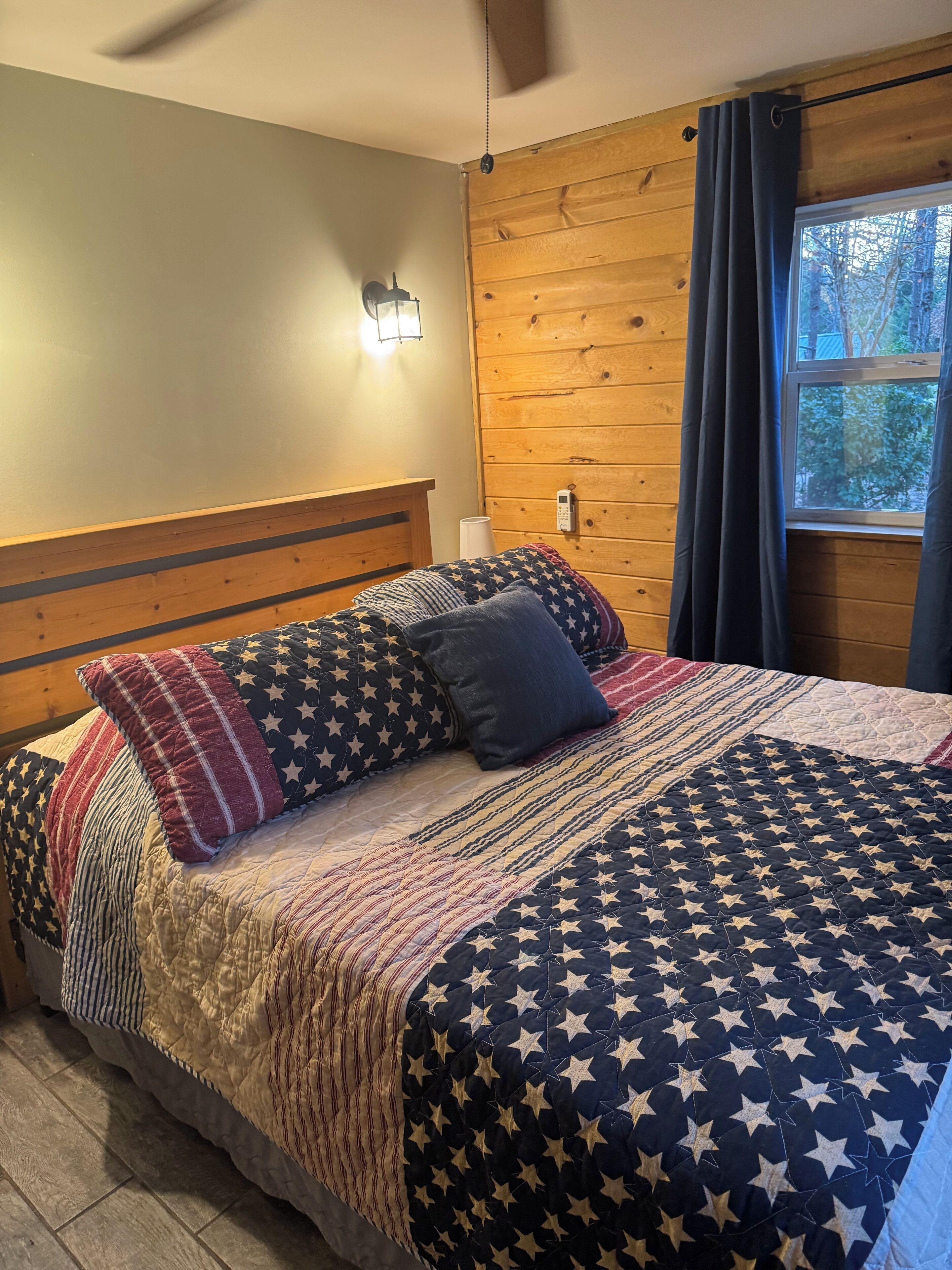 Ein Bett mit einer zudeckenen Decke mit Sternenmuster, einem Holzkopfstück und einem Nachttisch mit Lampe.
