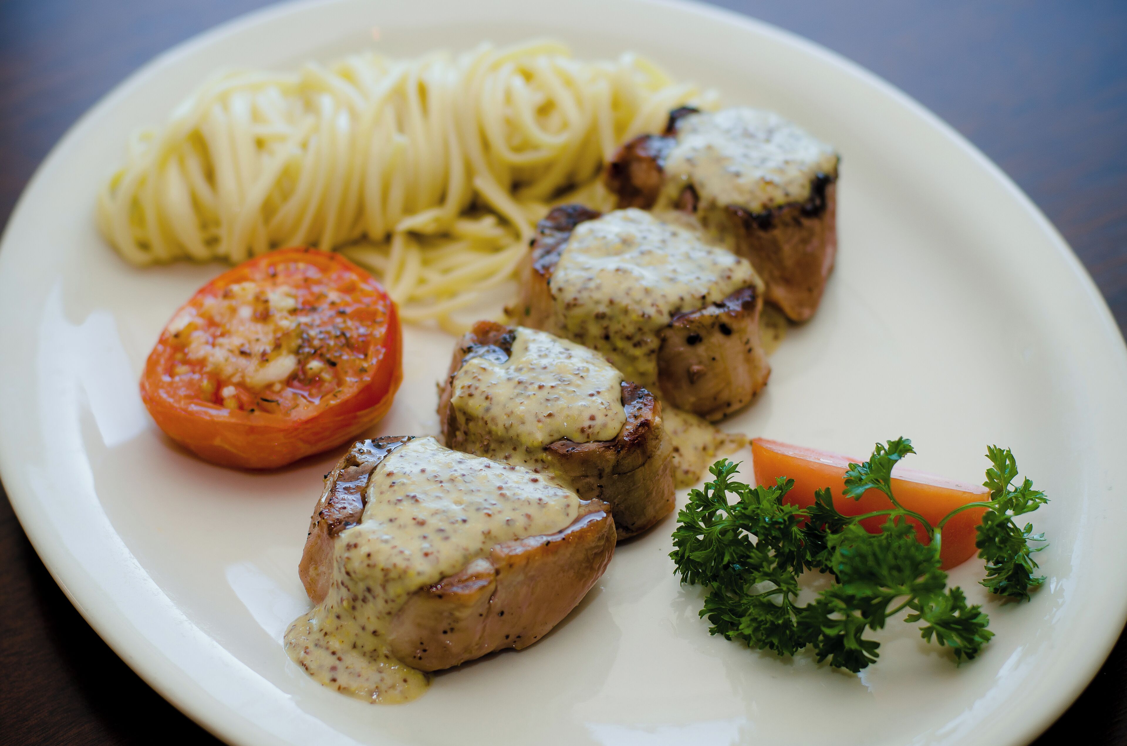 Une assiette contenant du poulet grillé, des spaghettis, une tranche de tomate et du persil.