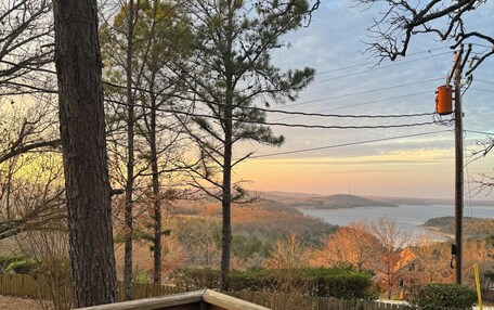 A wooden deck with a green bench, overlooking a scenic landscape with trees and a distant view of a body of water.