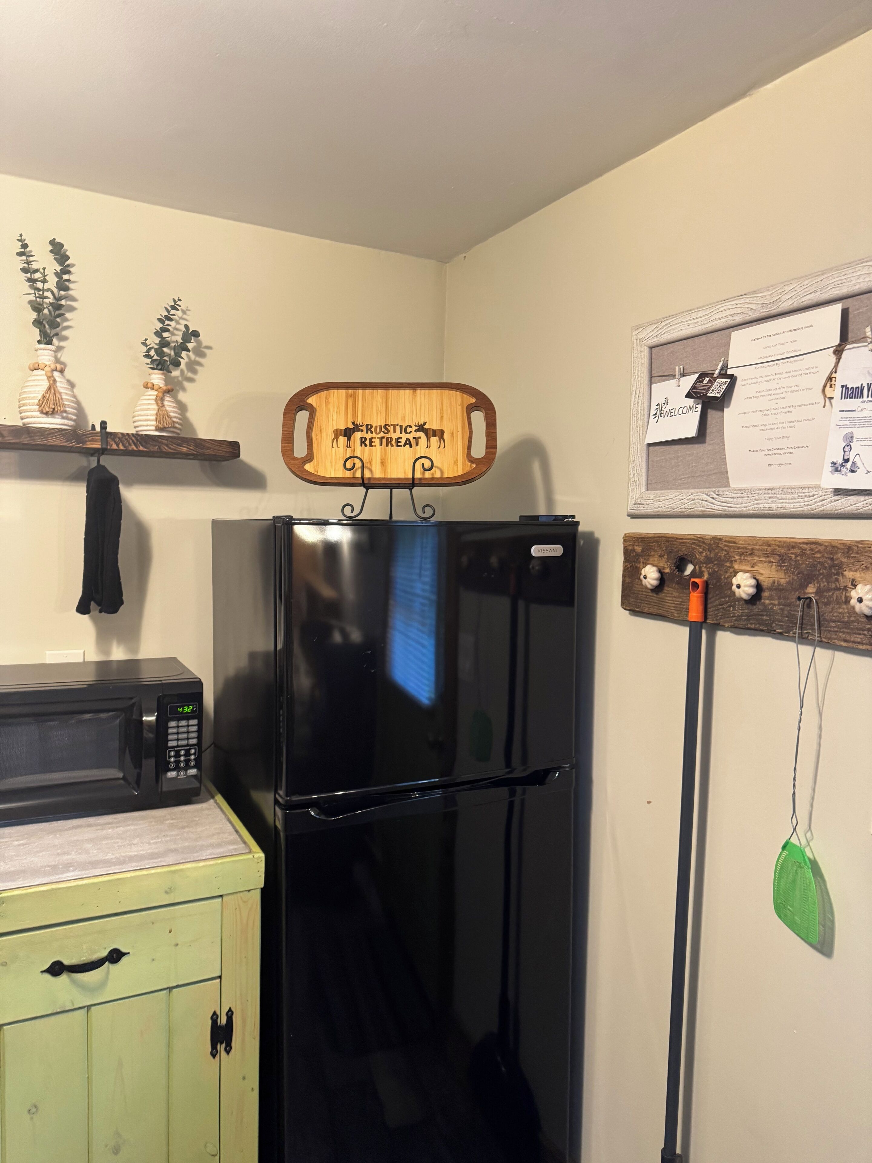 A kitchen with a black refrigerator, a microwave, and a wooden sign above the fridge that reads "Rustic Retreat".