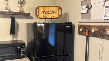 A kitchen with a black refrigerator, a microwave, and a wooden sign above the fridge that reads "Rustic Retreat".