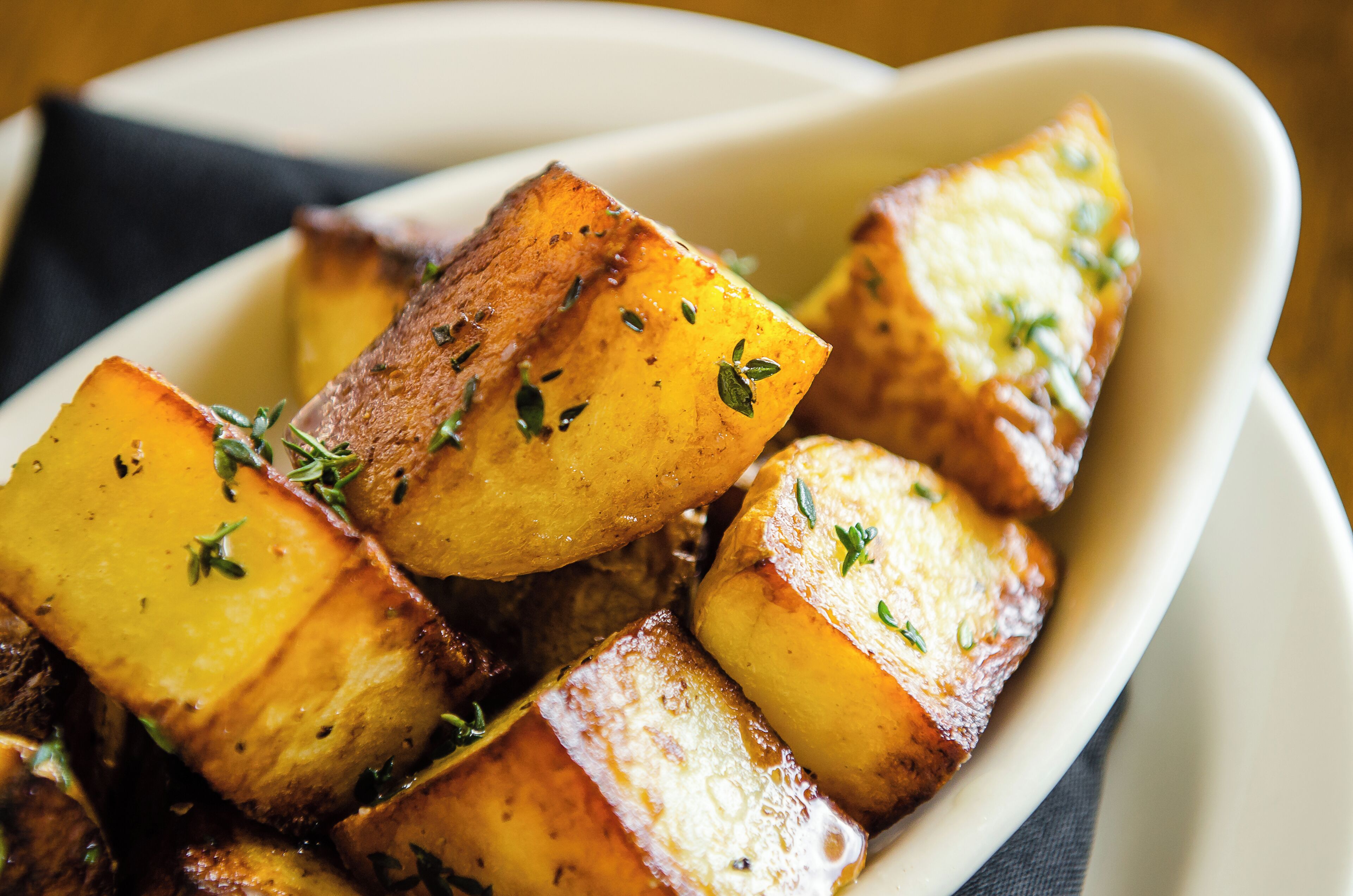 A white bowl filled with roasted potatoes garnished with herbs.