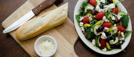 A wooden cutting board with a loaf of bread, a knife, and a small bowl of butter.