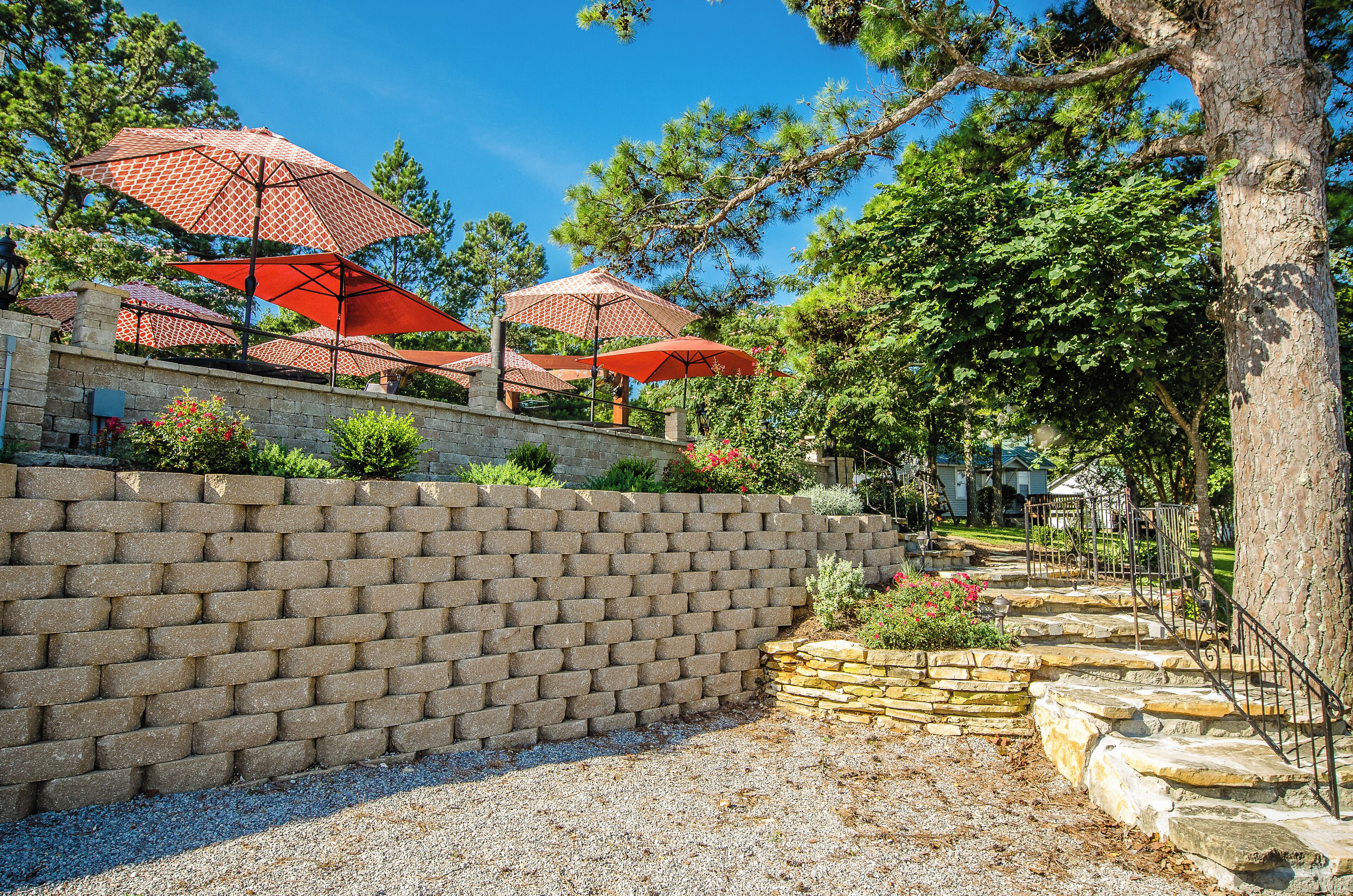 A brick wall with outdoor umbrellas, stone steps, and greenery.