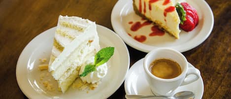 Two white plates with slices of cheesecake and a cup of coffee on a wooden table.