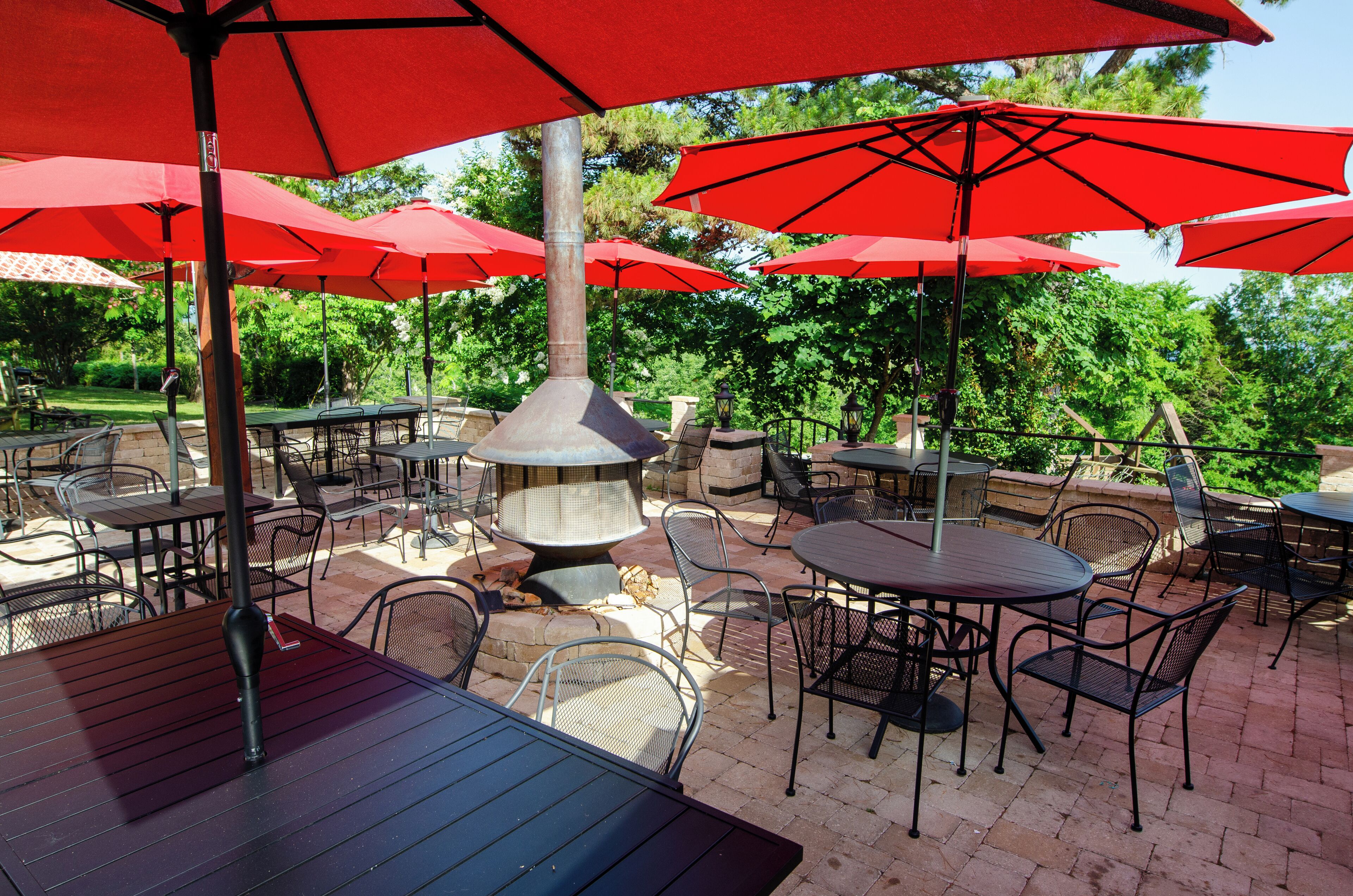 An outdoor patio with red umbrellas, metal chairs, and a central fire feature.