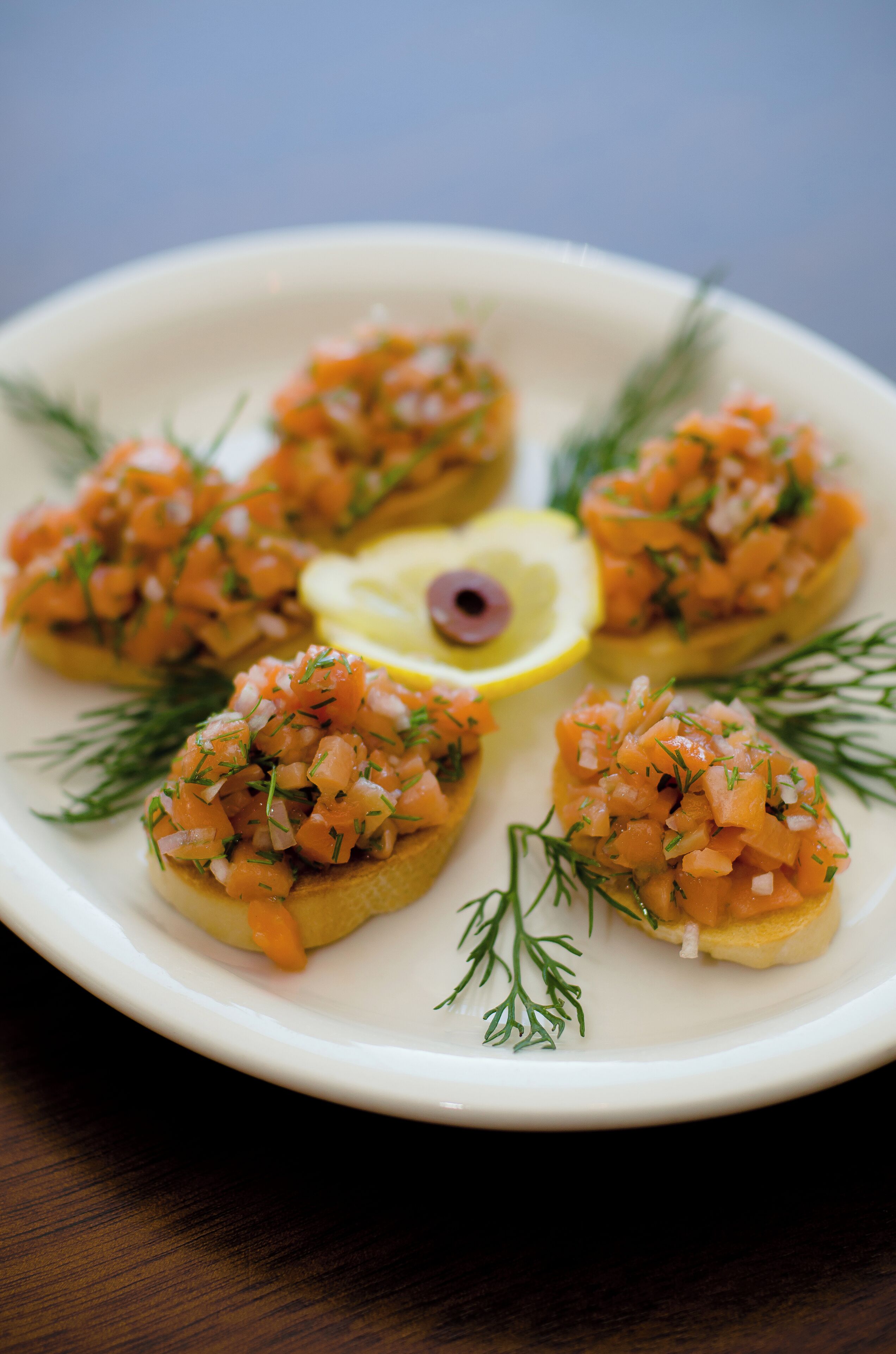 A plate of appetizers with a slice of lemon and dill garnish.