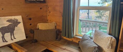 Tunnelmallinen ja maalaishenkinen huone, jossa on puinen penkki, hirven kuva, kyltti, jossa lukee ”Rustic Retreat”, ja ikkuna, josta avautuu näkymä puihin.