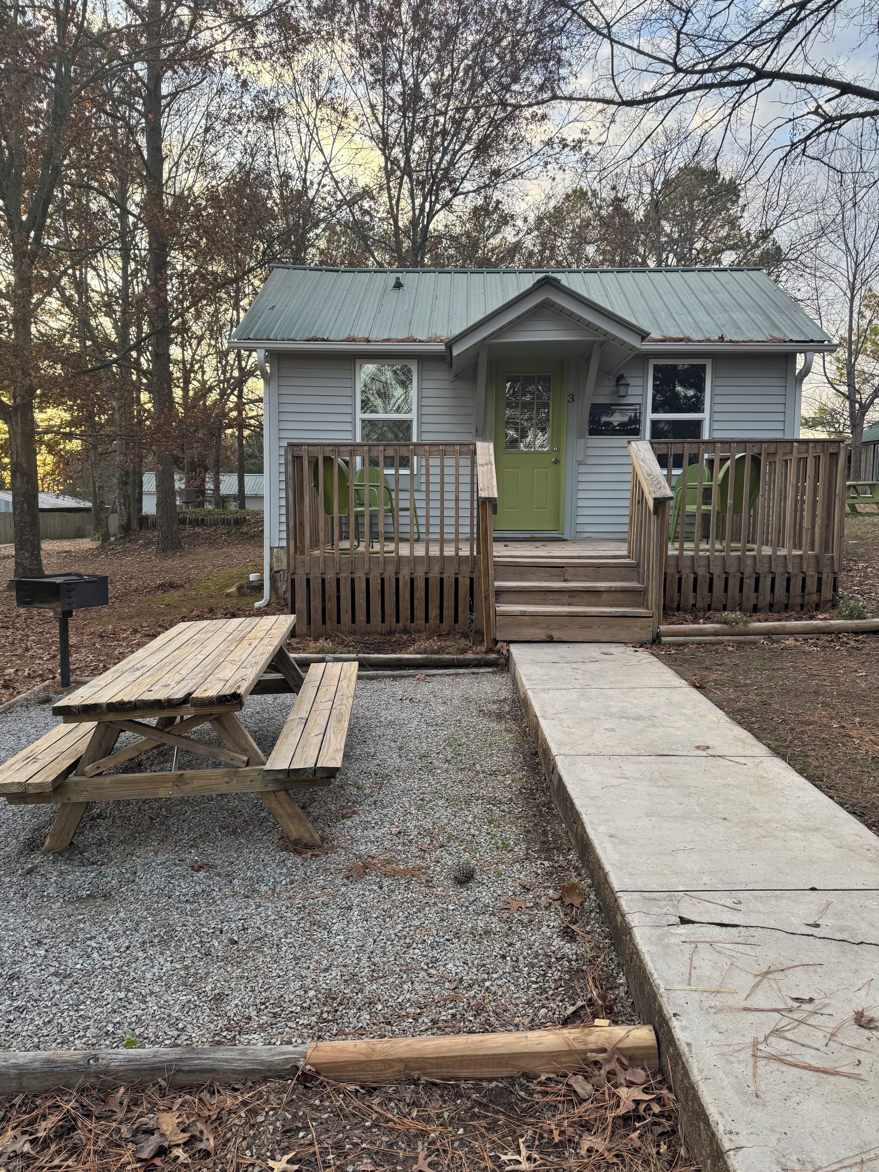 A small cabin with a green door, a wooden deck, and a picnic table.