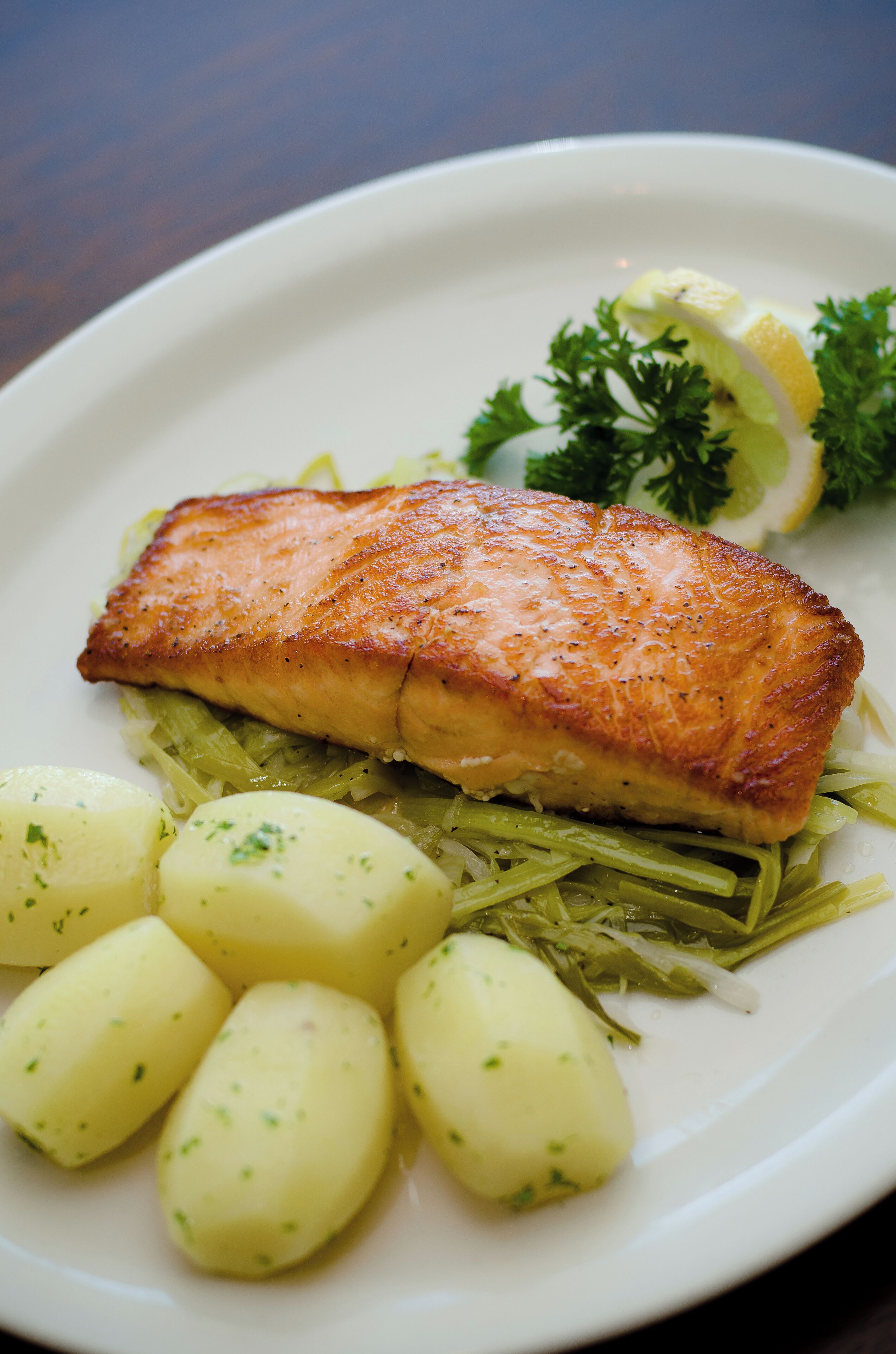 Un plato con un trozo de pescado cocido, patatas hervidas y una guarnición de perejil y limón.