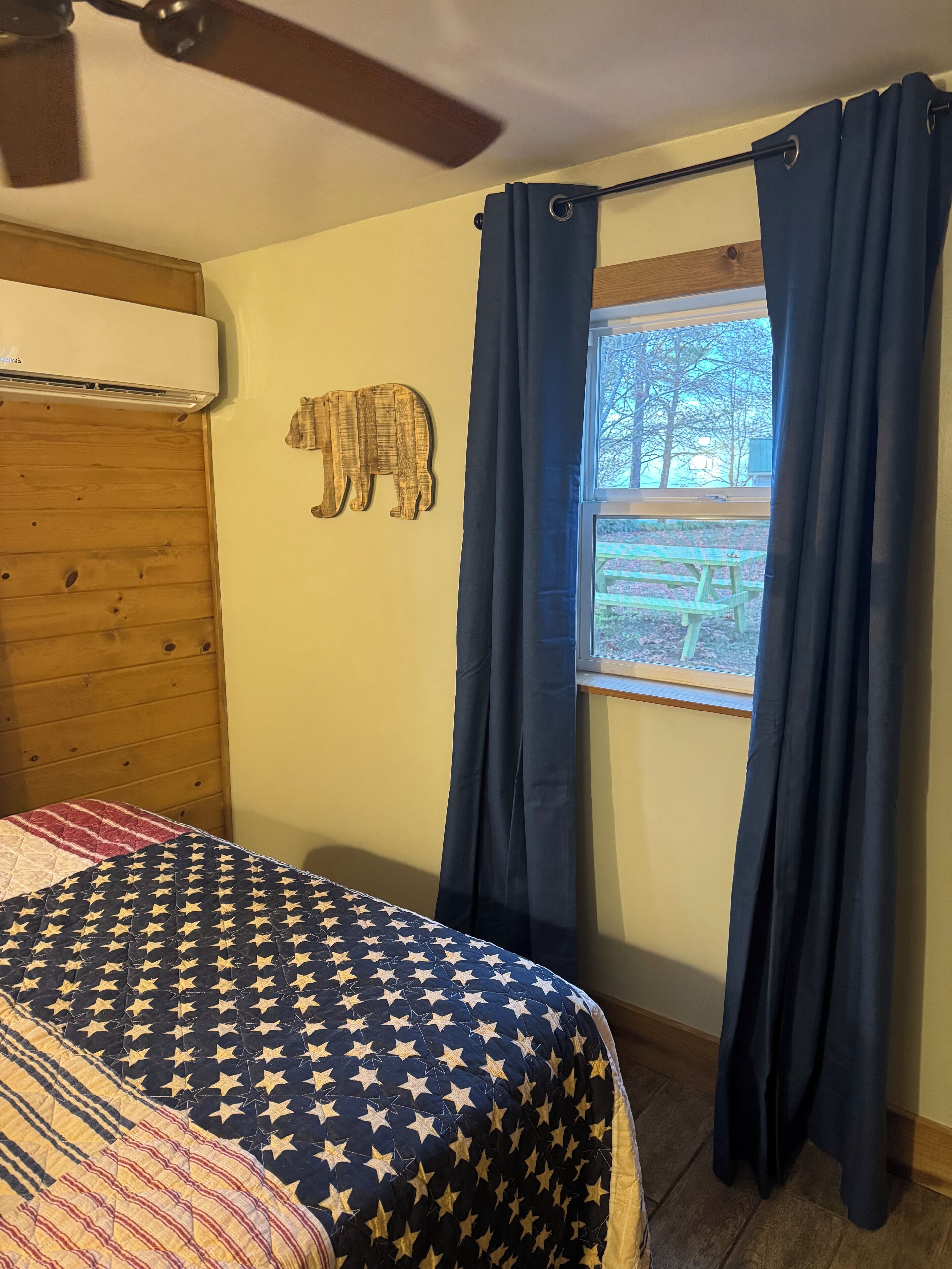Un dormitorio con cama, ventilador de techo, decoración de pared de madera y ventana con cortinas.