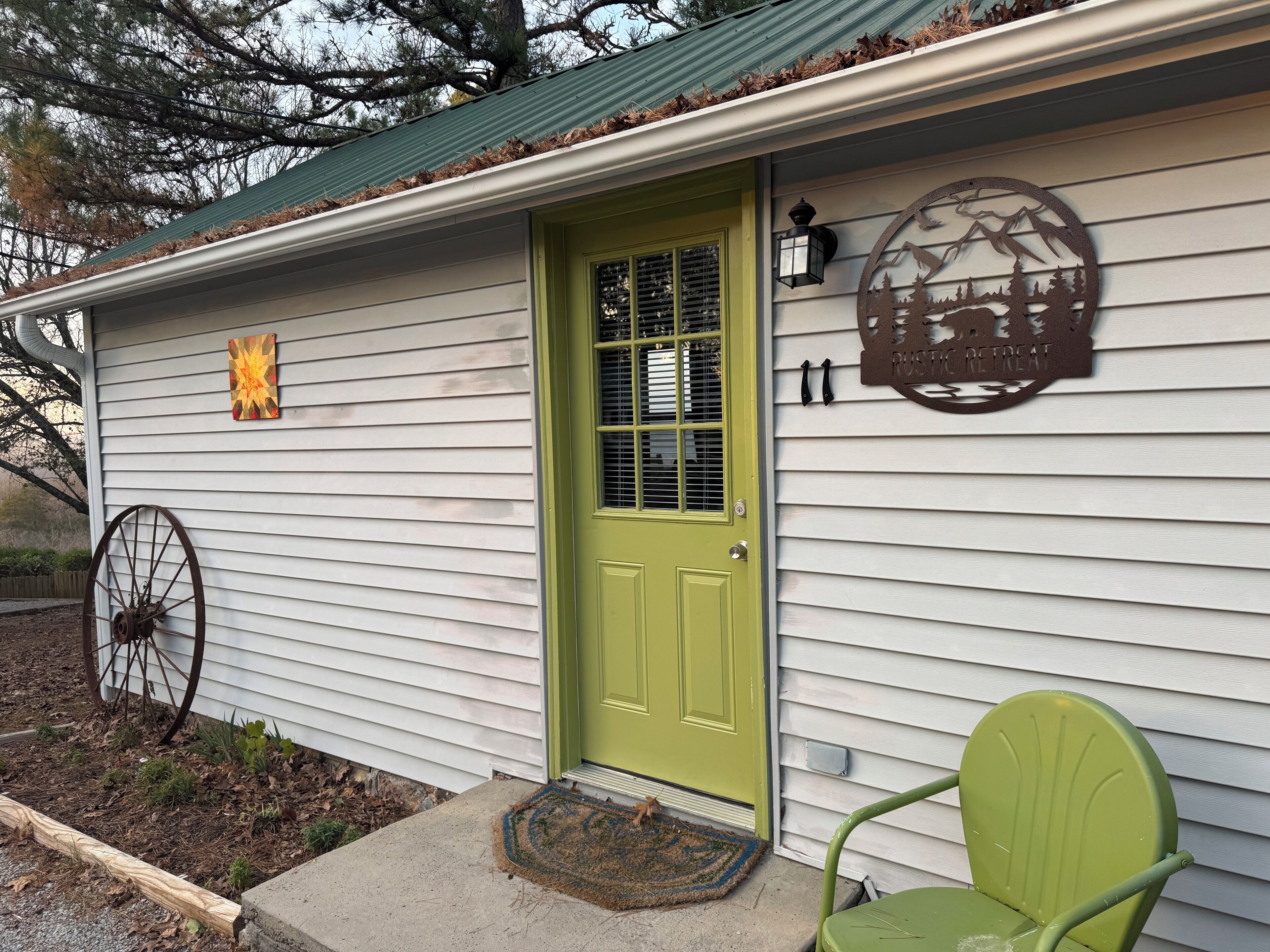 A rustic retreat with a green door, a metal sign with a mountain design, and a wheel chair outside.