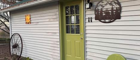 A rustic retreat with a green door, a metal sign with a mountain design, and a wheel chair outside.