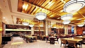 A spacious restaurant with high ceilings, wooden paneling, and multiple hanging light fixtures. Tables are arranged in a U-shape, and there are several seating areas with different chair styles. - Blue Bay Hotel (Zhangjiajie)