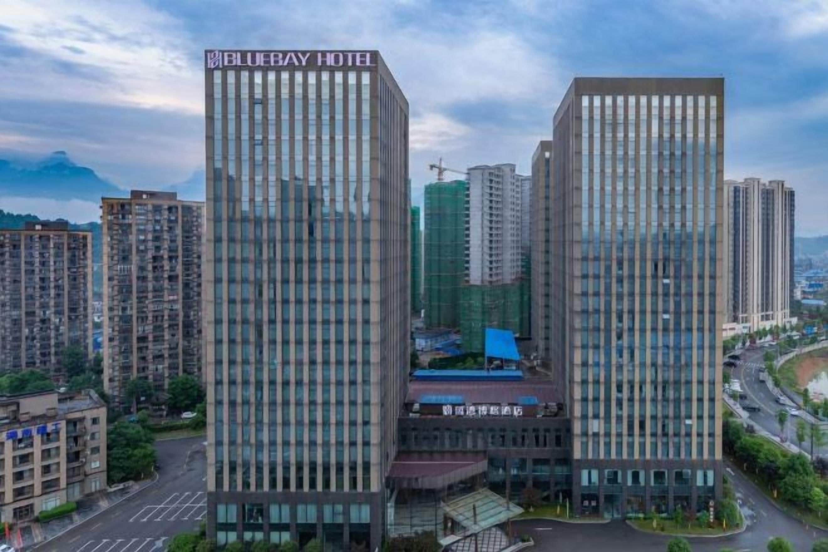 A modern hotel with a prominent sign, surrounded by high-rise buildings and a busy street.