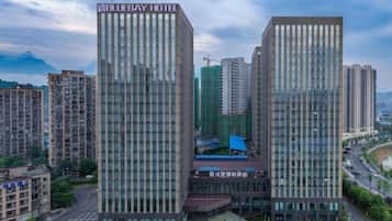 A modern hotel with a prominent sign, surrounded by high-rise buildings and a busy street.