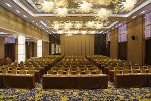Un salón de conferencias con filas de mesas y sillas, una alfombra estampada y un techo decorativo.