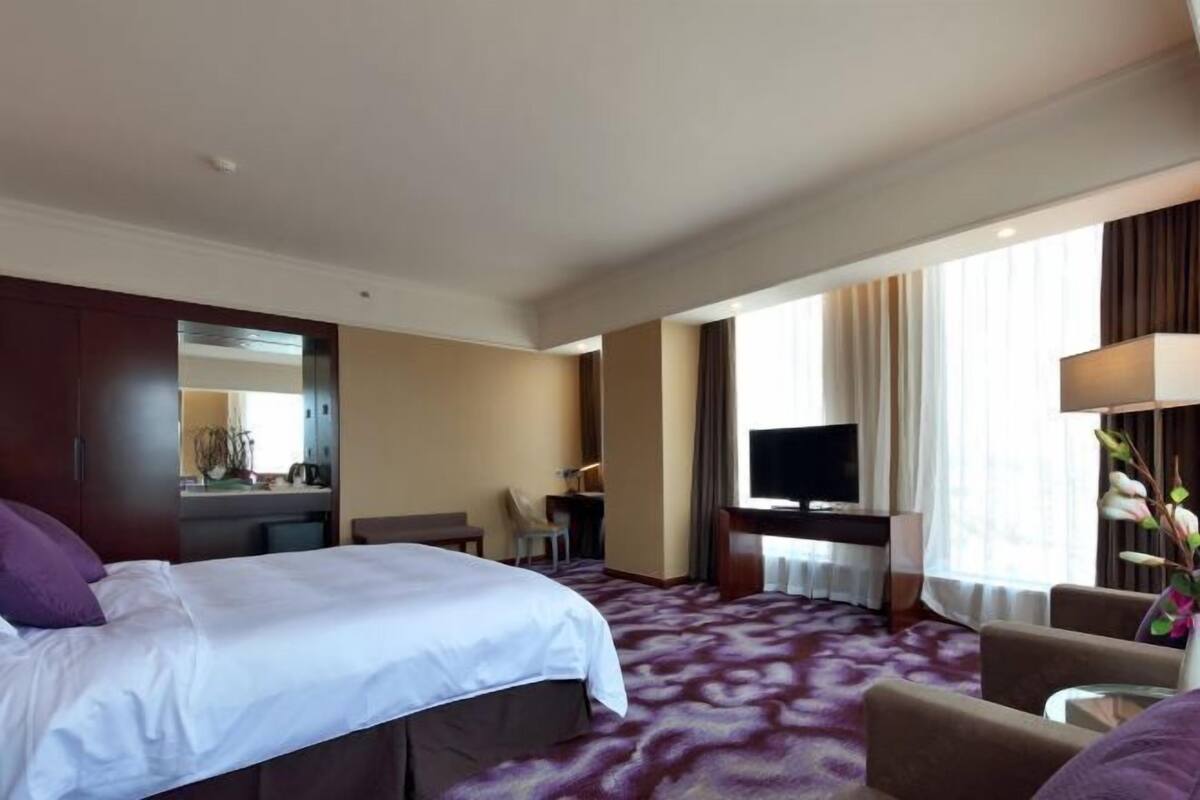 Una habitación de hotel con una cama grande, un escritorio con televisor, una silla y un sofá.