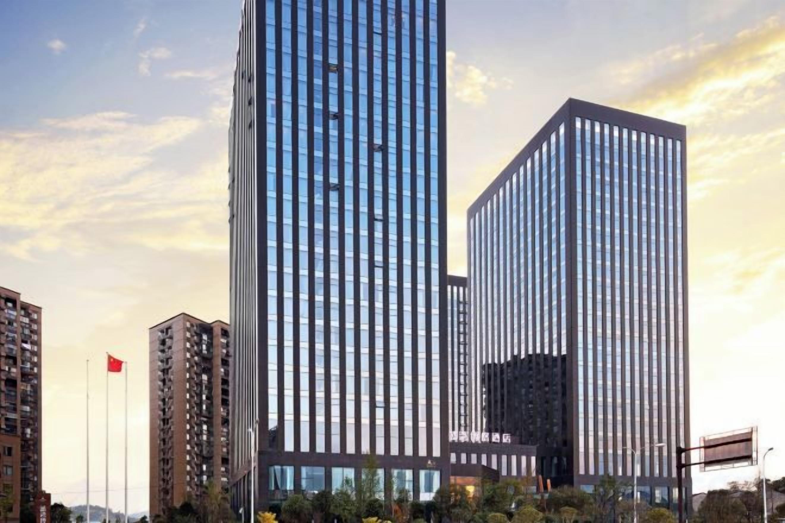 A modern high-rise building with a glass facade, surrounded by other buildings and a flag.