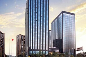 Un edificio moderno de gran altura con fachada de vidrio, rodeado de otros edificios y una bandera.