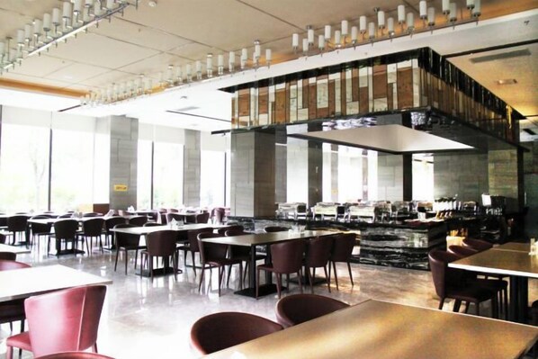 Un comedor amplio con varias mesas y sillas, una zona de bar central y ventanas grandes que proporcionan luz natural.