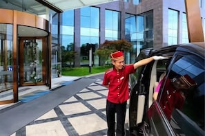A hotel entrance with a glass door, a parking area, and a modern building facade.