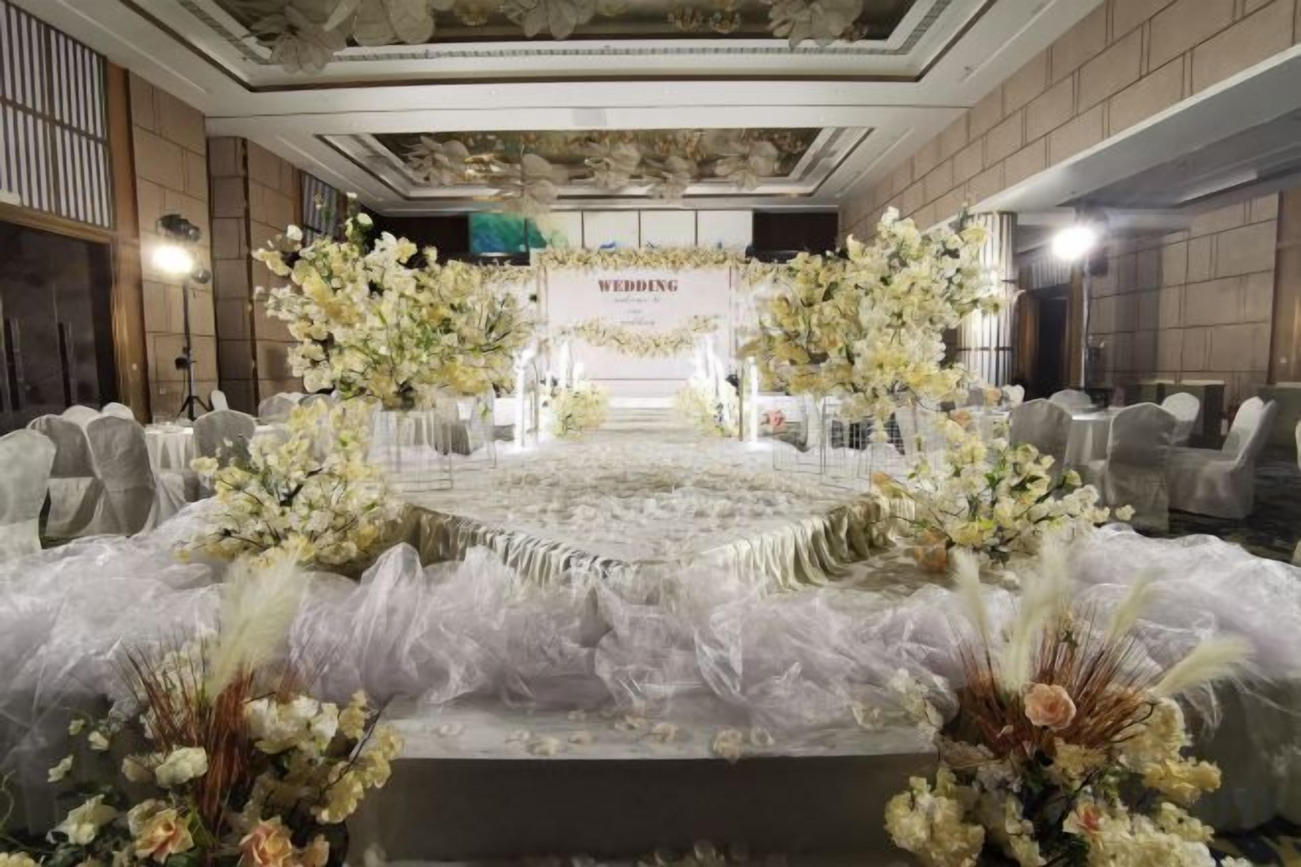 A wedding reception setup with a stage, floral arrangements, and seating.