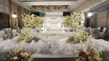 A wedding reception setup with a stage, floral arrangements, and seating.