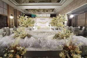 Aménagement d’une salle de réception pour un mariage, avec une scène, des décorations florales et des places assises.