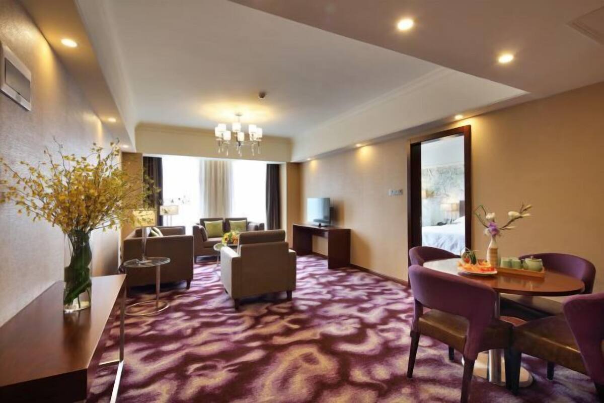 Habitación de hotel con sofá, sillones, mesa de comedor, televisor y un espejo grande.