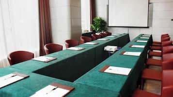Un salón de conferencias con una larga mesa, sillas rojas y una pantalla de proyector.