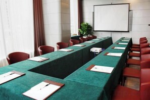 A conference room with a long table, red chairs, and a projector screen. - Blue Bay Hotel (Zhangjiajie)
