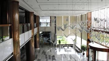 Un vestíbulo amplio con techo alto, ventanas grandes y una escalera central.