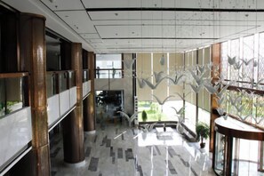 Un vestíbulo amplio con techo alto, ventanas grandes y una escalera central.