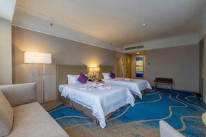 A hotel room with two beds, a sofa, a lamp, and a bench. - Blue Bay Hotel (Zhangjiajie)