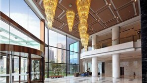 A spacious lobby with high ceilings, large chandeliers, and a glass facade offering views of the city. - Blue Bay Hotel (Zhangjiajie)
