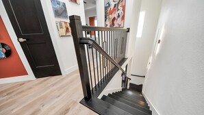 A modern staircase with a black handrail and wooden steps, leading to an upper floor.